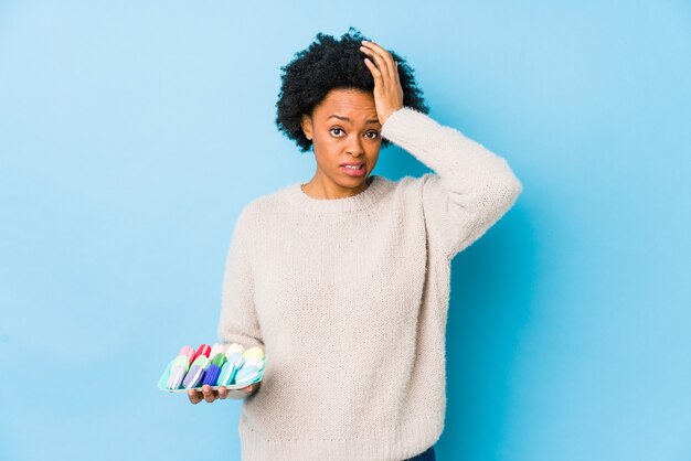 Femme afro-américaine d'âge moyen mangeant des macarons isolés étant choquée, elle s'est souvenue d'une réunion importante.