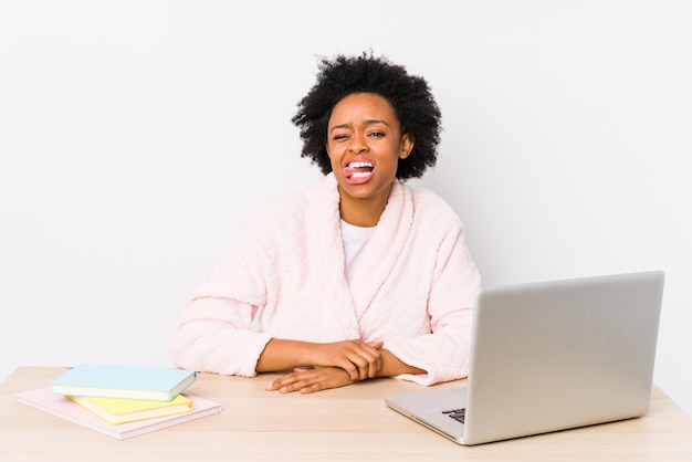 Femme afro-américaine d'âge moyen travaillant à la maison isolé drôle et sympathique qui sort la langue.