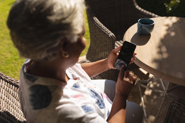 Femme afro-américaine âgée utilisant un smartphone dans un jardin ensoleillé. retraite, retraite et concept de style de vie senior heureux.