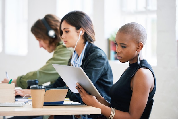 Femme afro-américaine à l'aide d'un ordinateur tablette numérique naviguant sur Internet assis à table travaillant avec des collègues