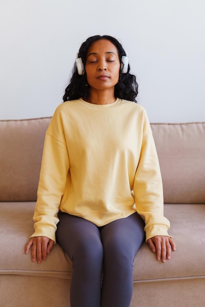 Femme afro-américaine assise sur le canapé et écoutant de la musique dans des écouteurs thérapie de respiration