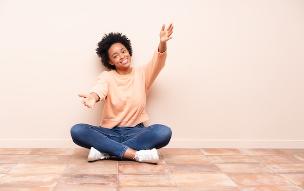 Femme afro-américaine assise sur le sol présentant et invitant à venir avec la main