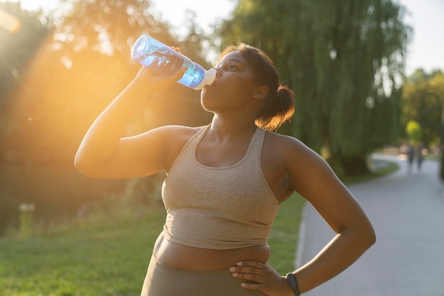 Une femme afro-américaine assoiffée buvant de l'eau pendant l'entraînement dans le parc