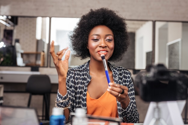 Femme afro-américaine aux cheveux bouclés à la recherche positive lors de l'enregistrement vidéo