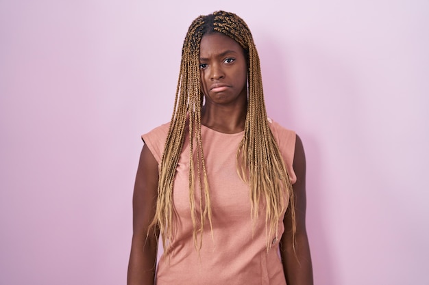 Femme afro-américaine aux cheveux tressés debout sur fond rose déprimée et inquiète pour la détresse, pleurant de colère et de peur. expression triste.