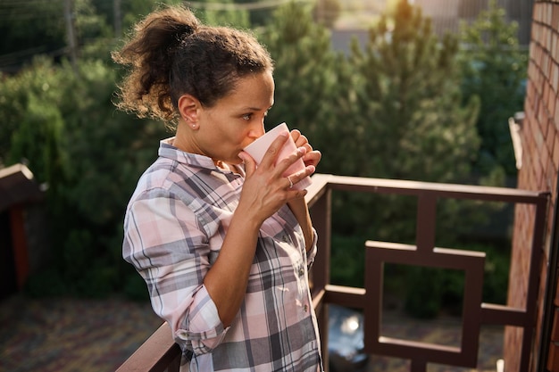 Une femme afro-américaine boit du café sur son balcon le jour de l'été