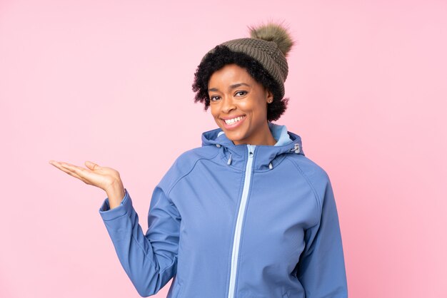 Femme afro-américaine avec chapeau d'hiver sur un mur rose isolé