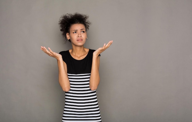Femme afro-américaine choquée avec les bras en l'air en pleine incrédulité. Portrait de jeune fille surprise, fond gris. Omg, wtf, concept d'émotions humaines