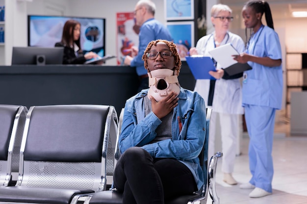 Femme afro-américaine avec collier de cou assis dans la salle d'attente de l'hôpital pour assister à l'examen de contrôle. Jeune adulte blessé ayant un rendez-vous de consultation avec un spécialiste au centre de santé.