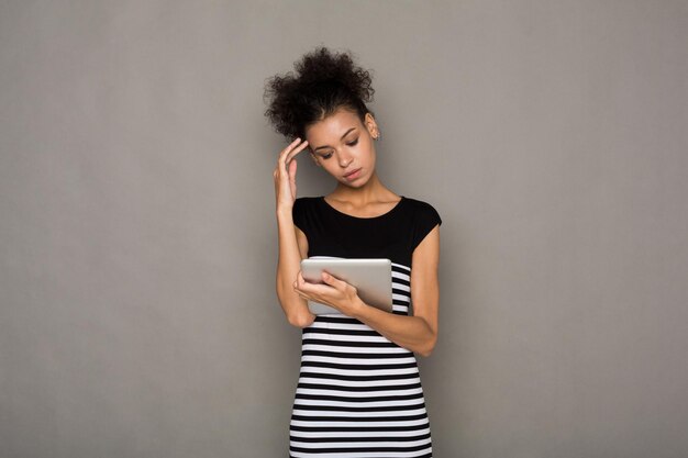 Femme afro-américaine concentrée à l'aide d'une tablette numérique sur fond gris. Notion de communication