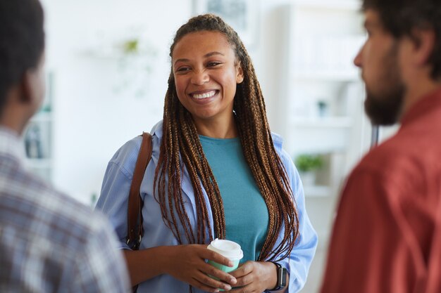 femme afro-américaine contemporaine souriant joyeusement tout en parlant à des amis ou collègues à l'intérieur