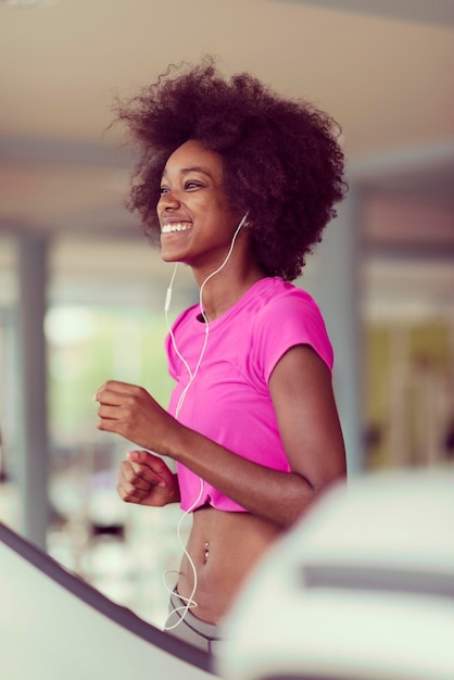 femme afro-américaine courant sur un tapis roulant à la salle de sport tout en écoutant de la musique sur des écouteurs