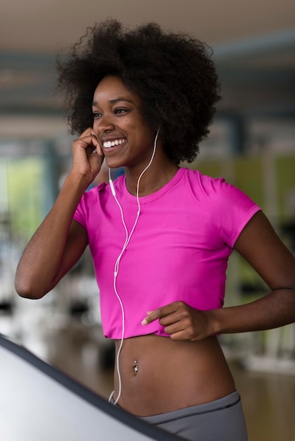 femme afro-américaine courant sur un tapis roulant à la salle de sport tout en écoutant de la musique sur des écouteurs