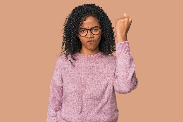 Une femme afro-américaine dans un studio montrant un poing à la caméra une expression faciale agressive