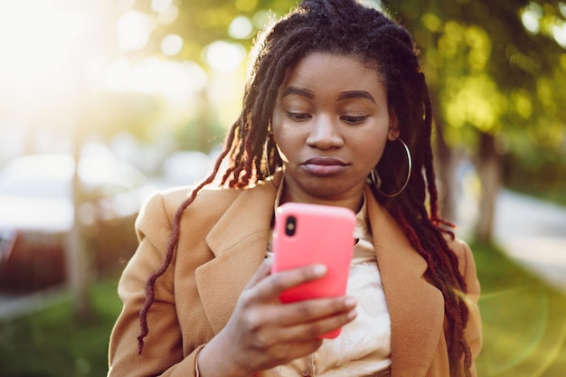 Femme afro-américaine debout dans une rue et utilisant un smartphone