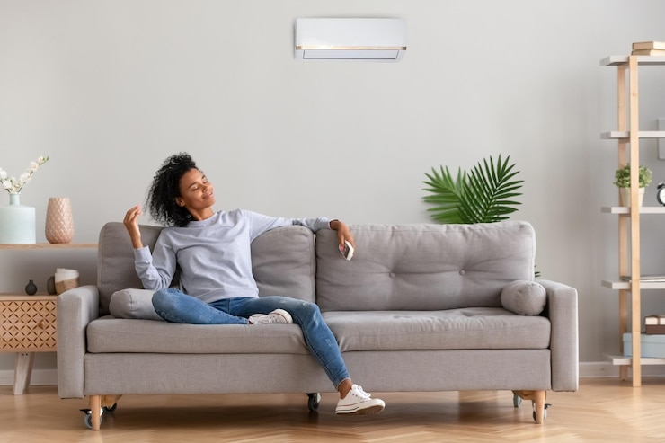 Photo une femme afro-américaine détendue assise sur un canapé confortable dans le salon d'une maison moderne tient une télécommande de climatiseur appréciant de respirer de l'air frais et frais en été ou l'air chaud en hiver