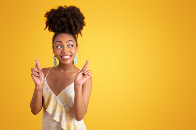 Une femme afro-américaine du millénaire positive en robe fait le signe des doigts croisés.