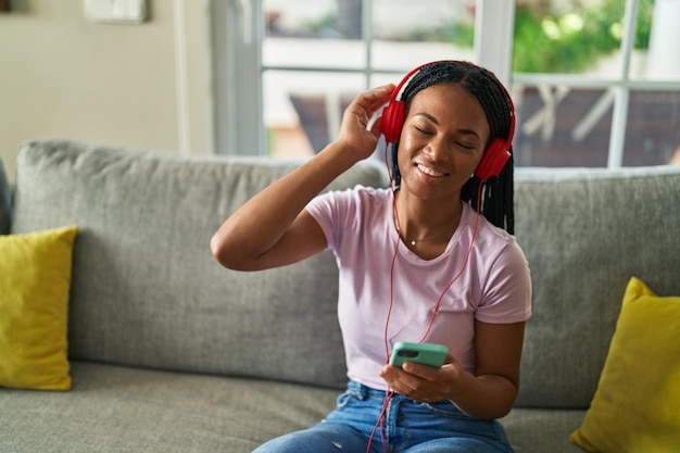 Femme afro-américaine écoutant de la musique assise sur un canapé à la maison