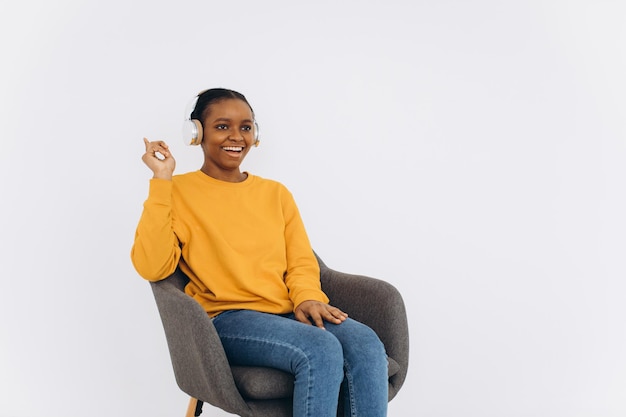 Une femme afro-américaine écoutant de la musique à travers des écouteurs à la maison montre quelque chose dans un espace de copie