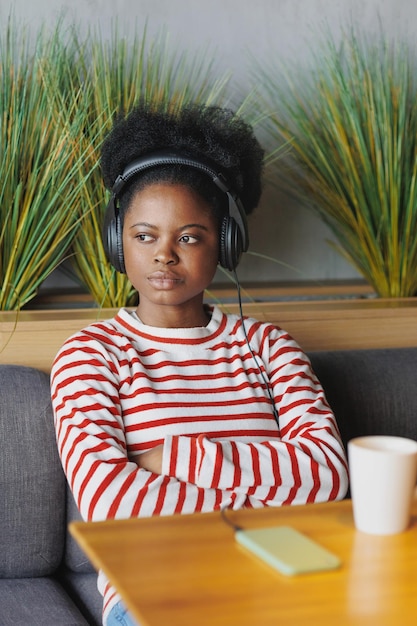 Une femme afro-américaine écoute des podcasts ou de la musique avec des écouteurs de son smartphone dans un public