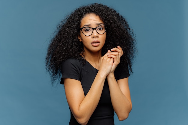 Une femme afro-américaine embarrassée garde les mains ensemble, regarde nerveusement la caméra