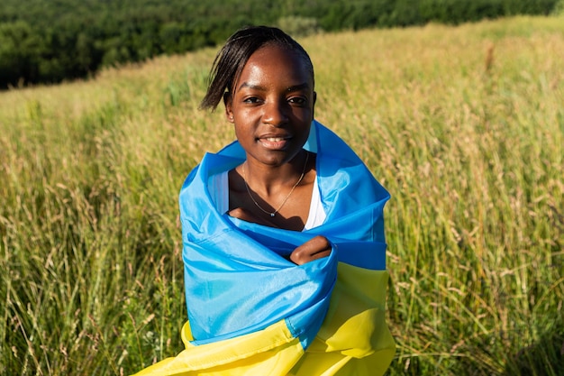 Femme afro-américaine enveloppée dans le drapeau bleu jaune ukrainien symbole national de l'Ukraine