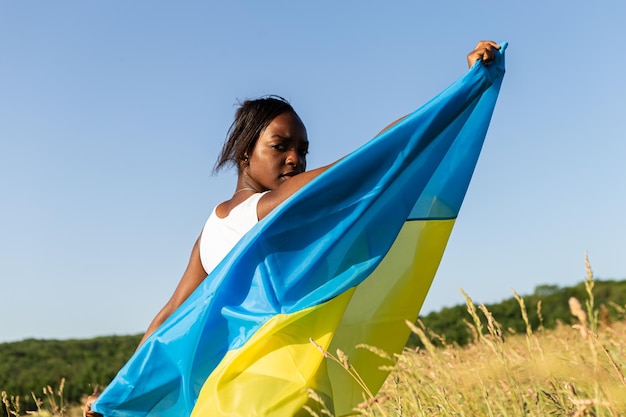 Femme afro-américaine enveloppée dans le drapeau bleu jaune ukrainien symbole national de l'Ukraine