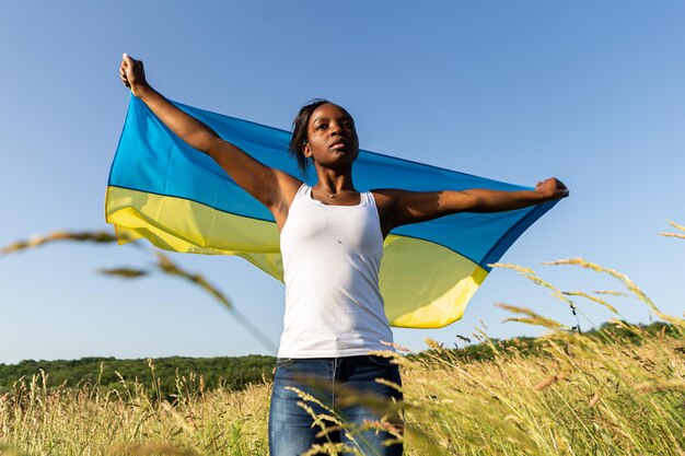 Femme afro-américaine enveloppée dans le drapeau bleu jaune ukrainien symbole national de l'Ukraine