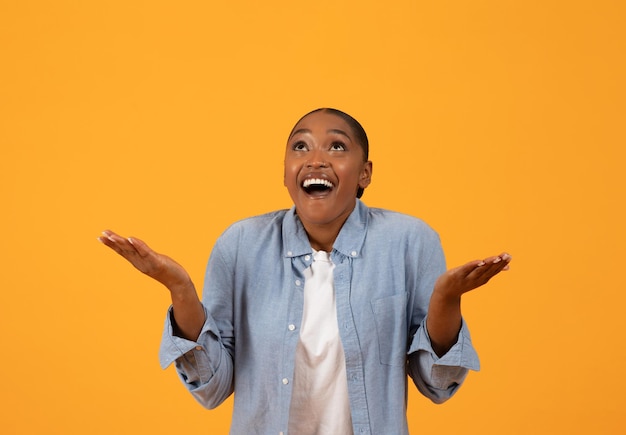 Une femme afro-américaine excitée célèbre une offre spéciale sur un fond orange.