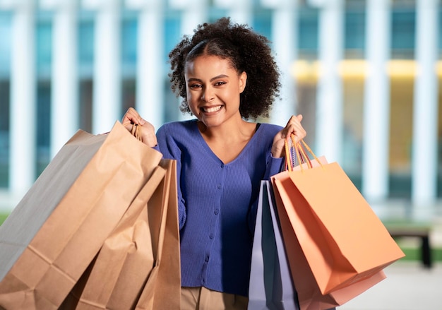 Femme afro-américaine excitée posant avec des sacs en papier à l'extérieur