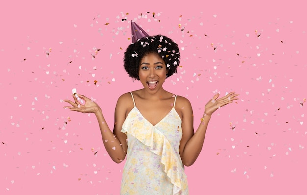 Une femme afro-américaine extatique aux cheveux bouclés fête en portant un chapeau de fête.