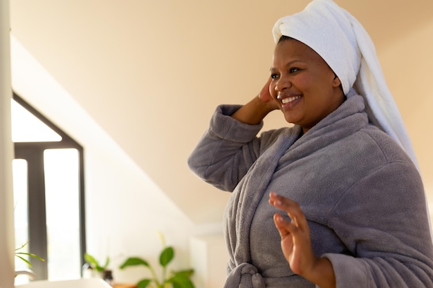 Photo une femme afro-américaine heureuse portant un peignoir se regarde dans le miroir de la salle de bain.