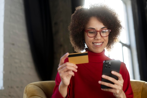 Photo une femme afro-américaine indépendante détenant un smartphone de carte de crédit reçoit un paiement travaillant à domicile