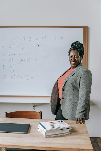 Femme afro-américaine joyeuse et confiante regardant la caméra près de la table avec des manuels en classe