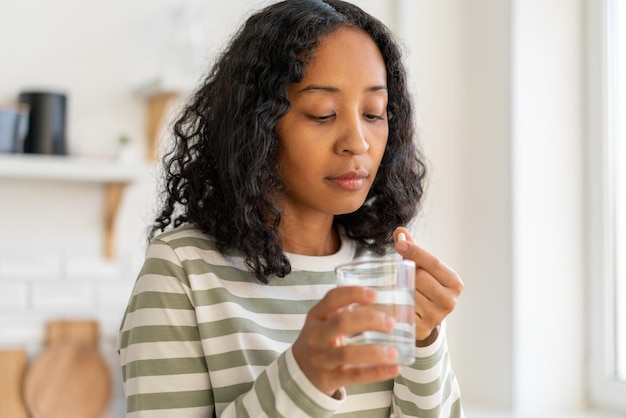 Photo femme afro-américaine laver la pilule avec un verre de traitement de remède supplément waterhealthy