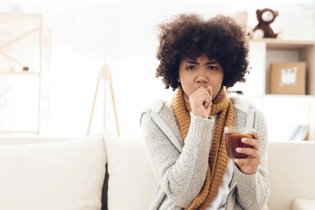 Femme afro-américaine malade avec froid assis sur un canapé.