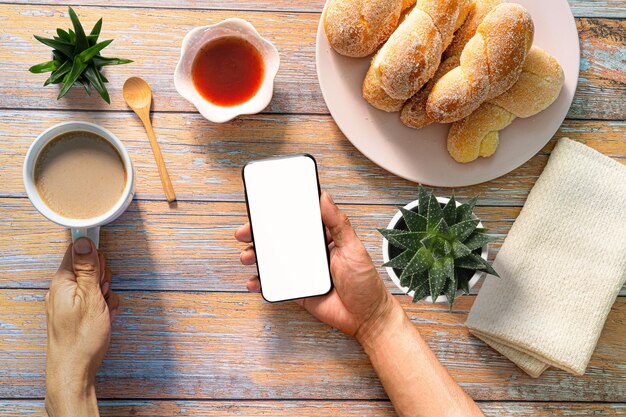 Femme afro-américaine méconnaissable utilisant un smartphone tout en prenant son petit-déjeuner avec un café au café