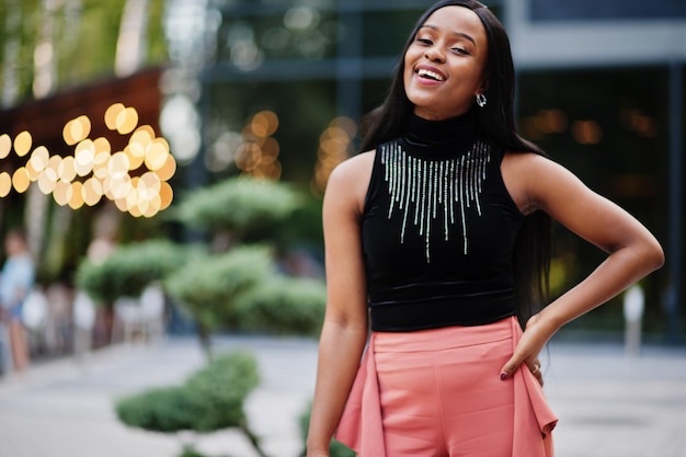 Femme afro-américaine à la mode en pantalon de pêche et chemisier noir pose en plein air.