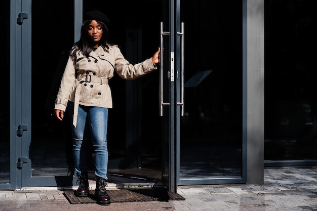 Une femme afro-américaine à la mode porte un béret et un manteau debout contre la porte.