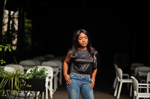 Une femme afro-américaine à la mode porte des jeans posant à l'extérieur.