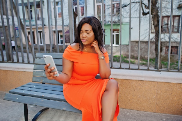 Femme afro-américaine modèle xxl en robe orange regardant sur téléphone mobile