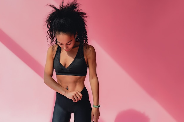 femme afro-américaine noire en leggings noirs et tenue de fitness supérieure sur rose