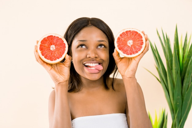 Femme afro-américaine avec un pamplemousse sur fond blanc, montrant sa langue. Beauté de la peau.