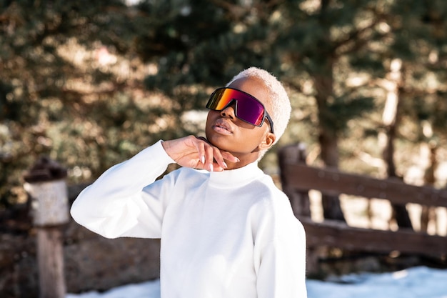 Une femme afro-américaine portant des lunettes de neige sur une montagne enneigée en hiver