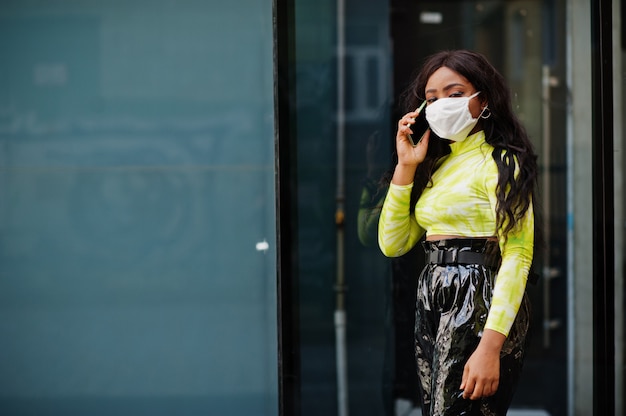 Femme afro-américaine posant avec un masque facial pour se protéger des infections contre les bactéries, les virus et les épidémies et tenir le téléphone mobile.