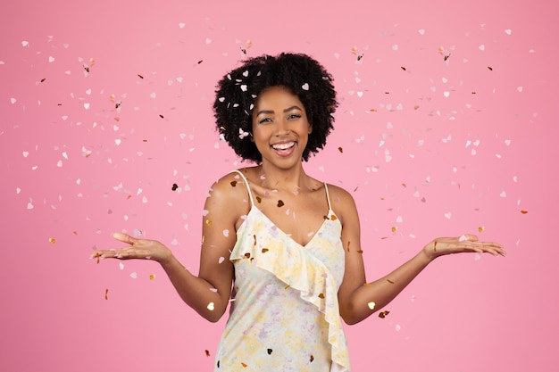 Une femme afro-américaine rayonnante aux cheveux bouclés rit joyeusement au milieu d'une pluie de confettis sur un