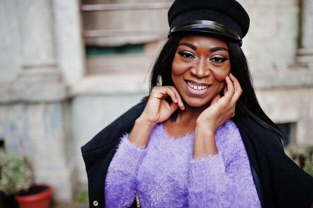 Femme afro-américaine en robe violette et casquette posée en plein air