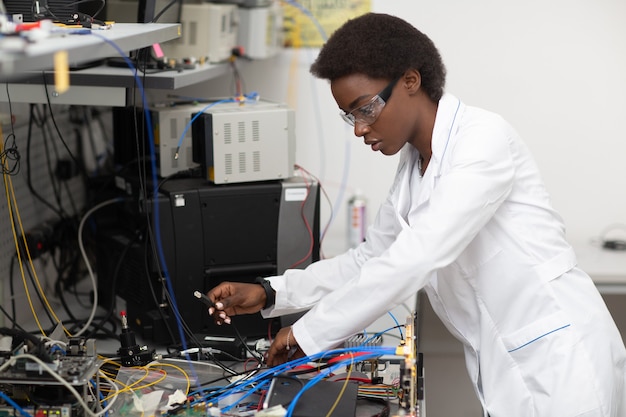 Femme afro-américaine scientifique travaillant en laboratoire avec un dispositif de cryptage à fibre optique de technologie électronique recherche et développement d'appareils électroniques par couleur femme noire