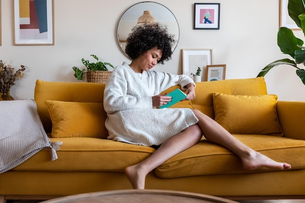 Femme afro-américaine se détendre à la maison en lisant un livre assis sur un canapé Littérature et concept de style de vie