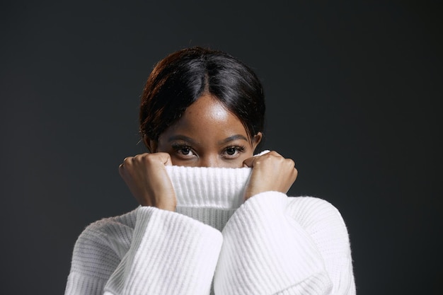 Photo femme afro-américaine sérieuse se cachant le visage derrière le col d'un chandail d'hiver confortable tricoté chaud et élégant